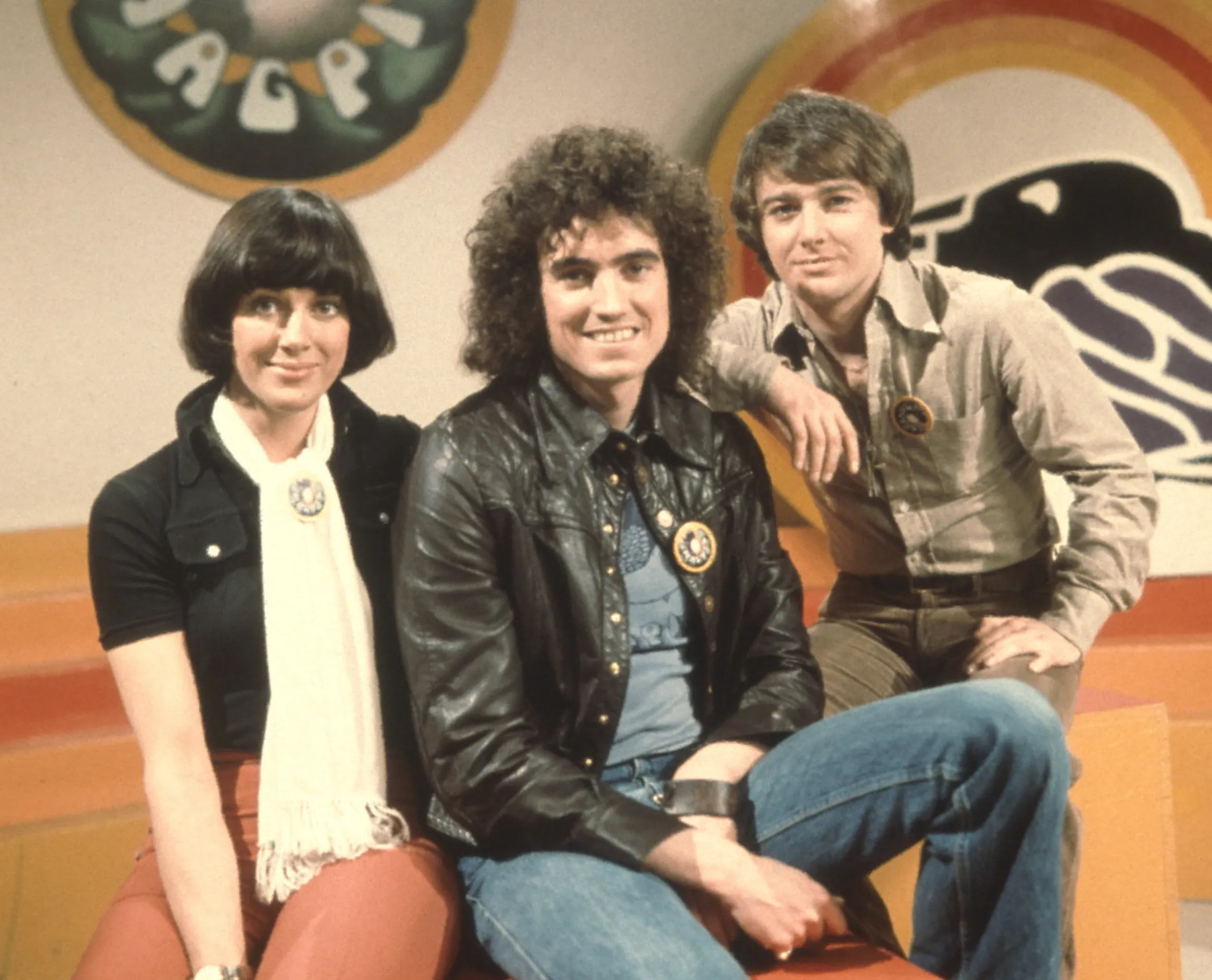 Susan Stranks, Mick Robertson, and Douglas Rae, presenters of the TV show "Magpie," pose on a colorful set.