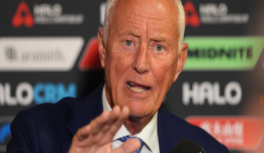 Barry Hearn holds his right hand out in front of him as he talks in a media conference, wearing a mostly light blue tie, white shirt and blue smart jacket