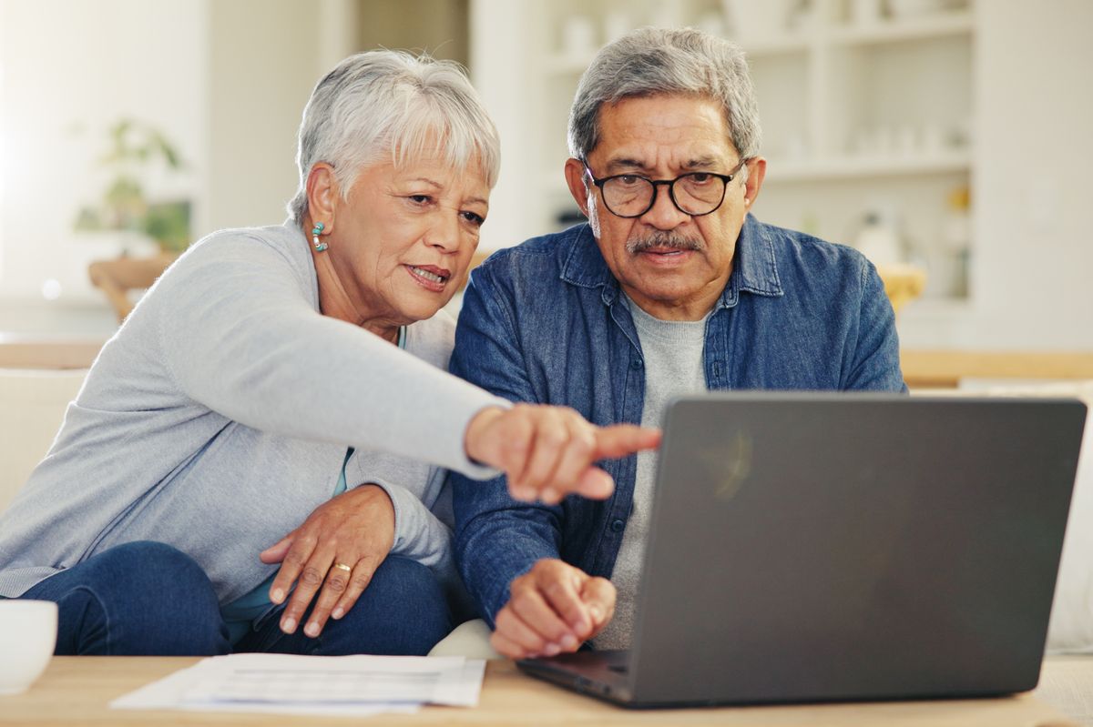 Senior, couple and pointing on laptop in living room with document for financial planning, investment or retirement. Elderly man, woman and technology for online banking, account balance or savings