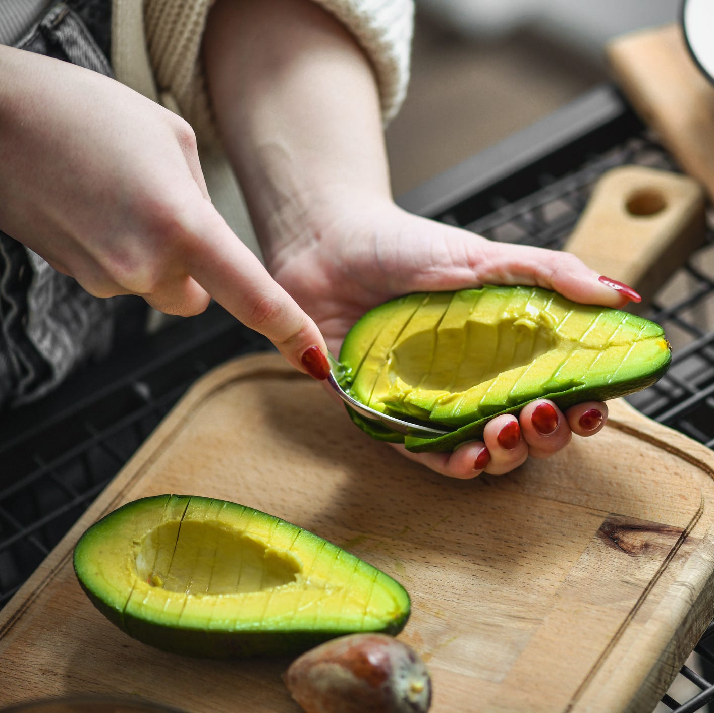 Female Using Spoon Method Removing Avocado Slices From Peel