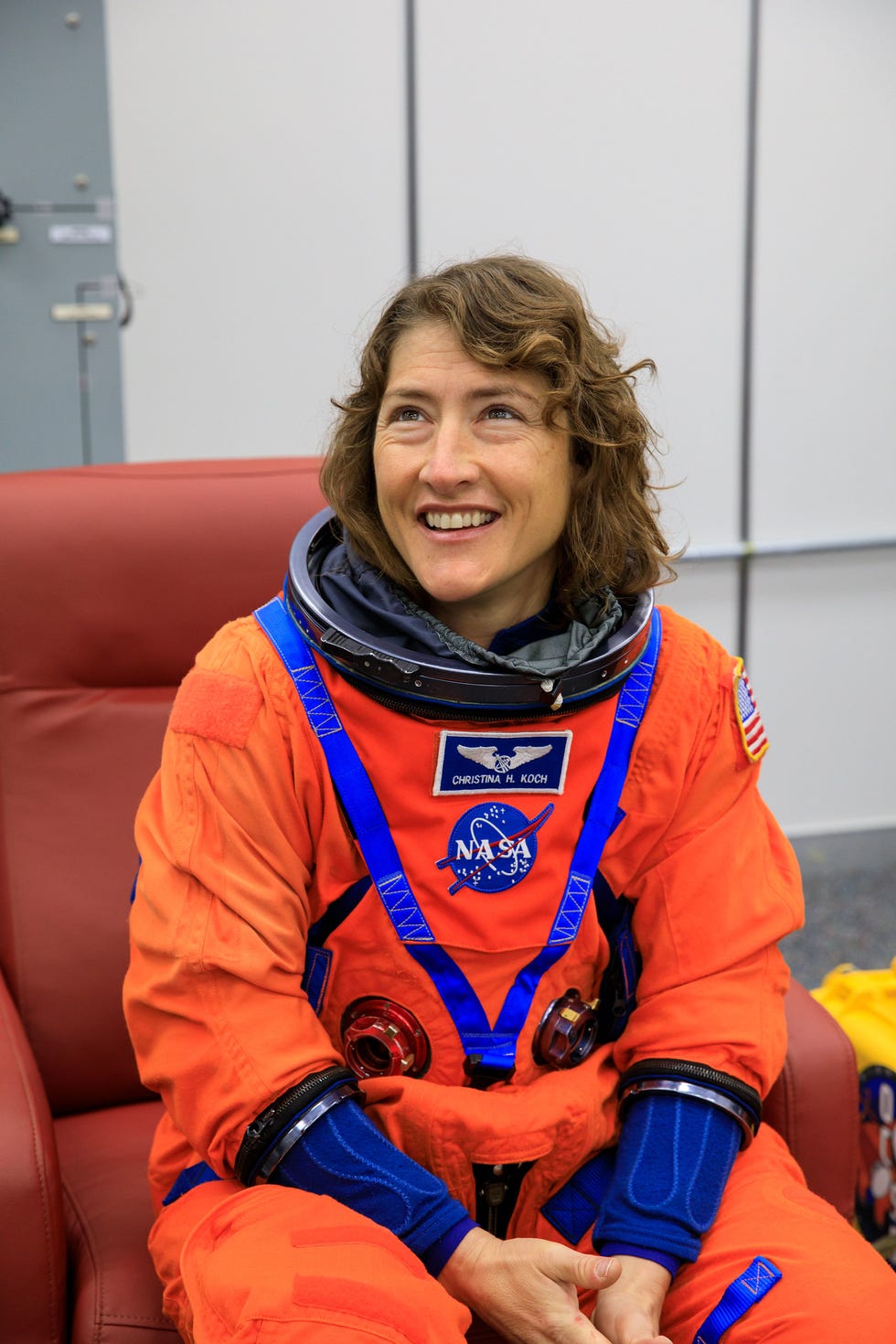 Astronaut dressed in an orange space suit seated in a chair.