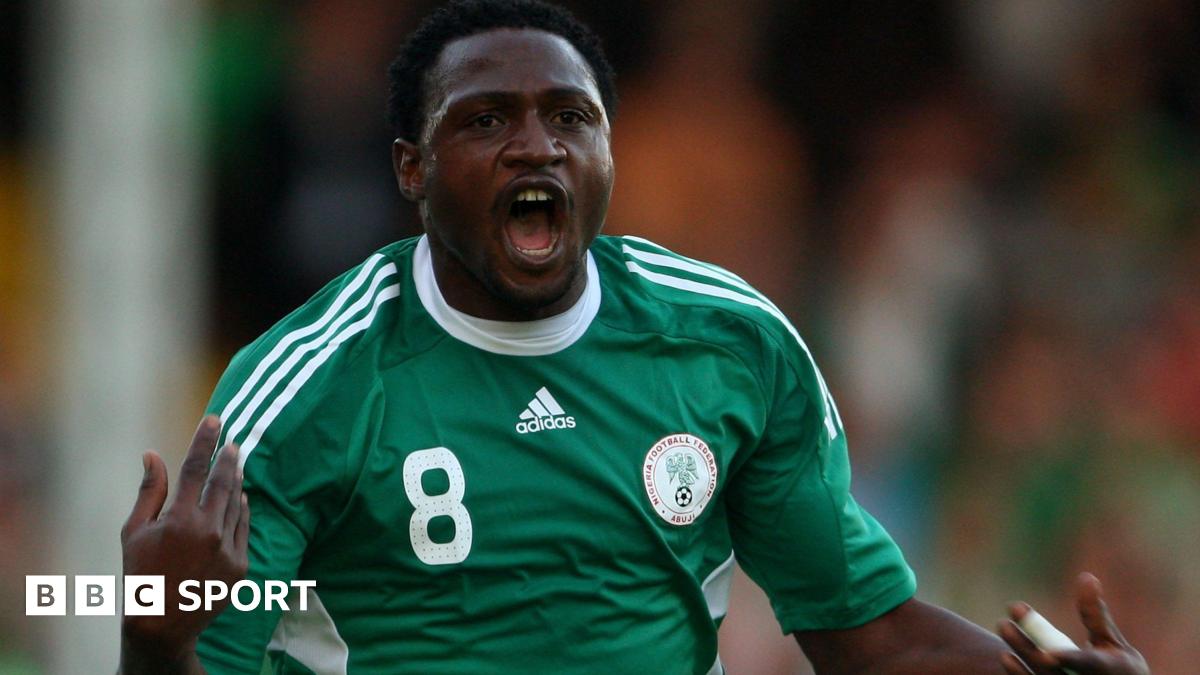 Michael Eneramo shown from waist up, wearing a green Nigeria shirt with white trim, the number eight on the right of his chest and Nigeria crest on the left, holds his hands up and is seen with his mouth open in celebration after scoring a goal