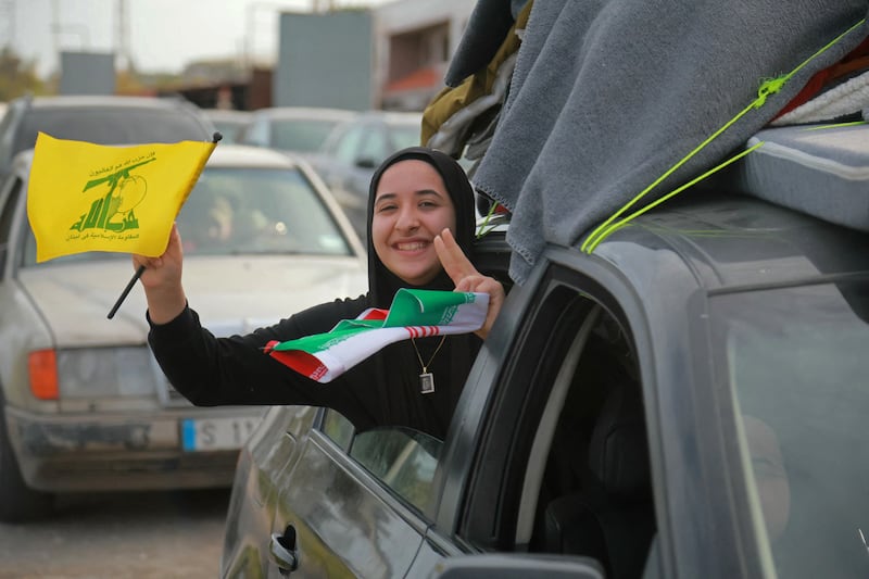 A displaced resident travels through the Qasmieh area while holding a flag of Hizbullah on the way back to her home in southern Lebanon on Friday. Photo by Ibrahim Amro/AFP via Getty Images