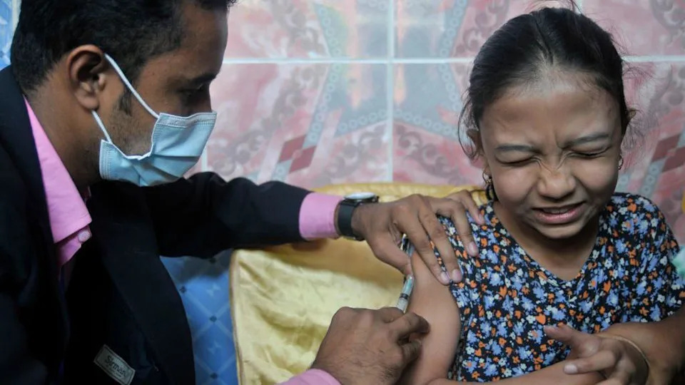 A man inserting the needle of a syringe into the arm of a young girl.