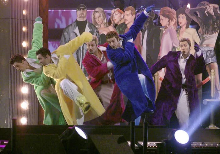 Group of male performers on stage in colorful coats, dancing energetically with a dynamic background poster