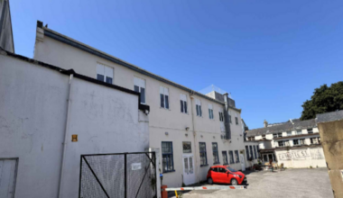 A large white building around a courtyard with one red car parked outside