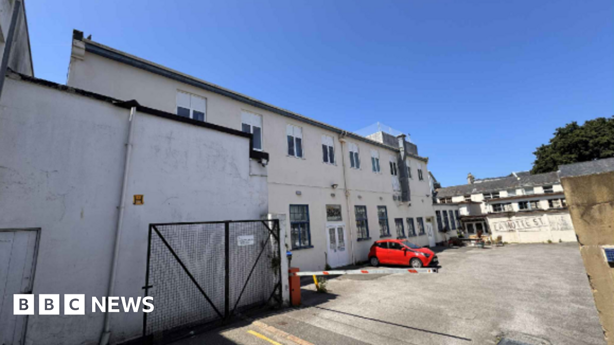A large white building around a courtyard with one red car parked outside