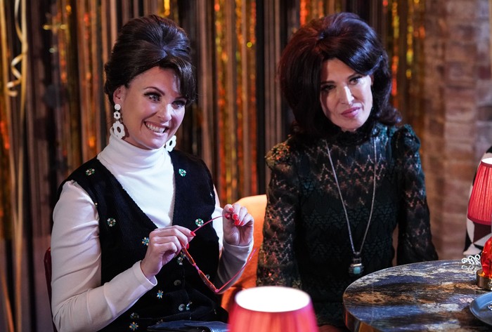 Bea and Honey sit in 60s style wigs and clothing in a scene from EastEnders