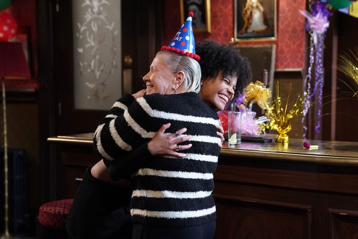 557192,TITLE:Eastenders Mo, in a party hat, hugs Jasmine in a scene from EastEnders