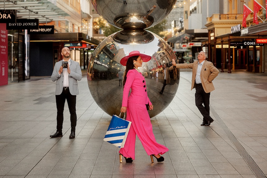 Two silver spheres on top of each other in a mall with three people around them