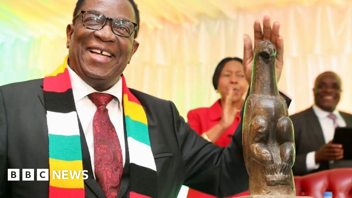 Emmerson Mnangagwa wears a scarf bearing Zimbabwe's national colours. He smiles next to one of the stone bird sculptures.