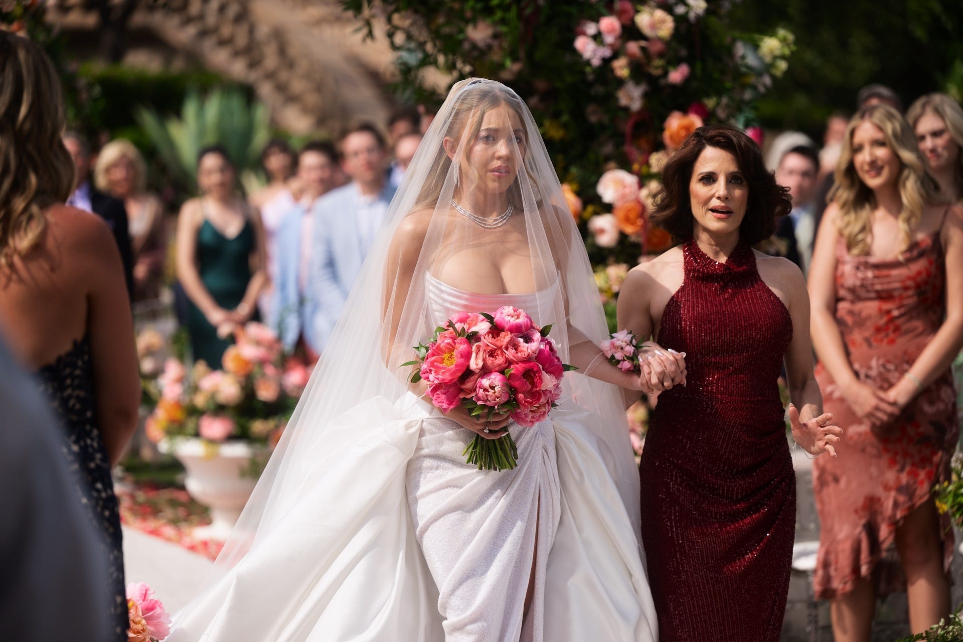 Bride in a wedding dress holding a bouquet, walking down an aisle.