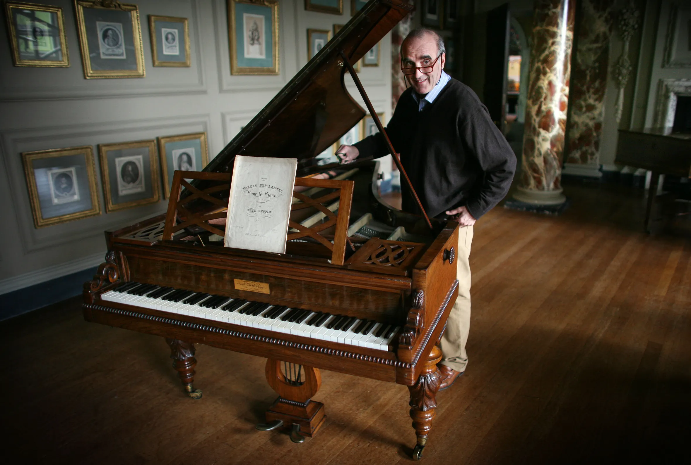 Alec Cobbe stands beside a piano that once belonged to Chopin, holding open the lid.