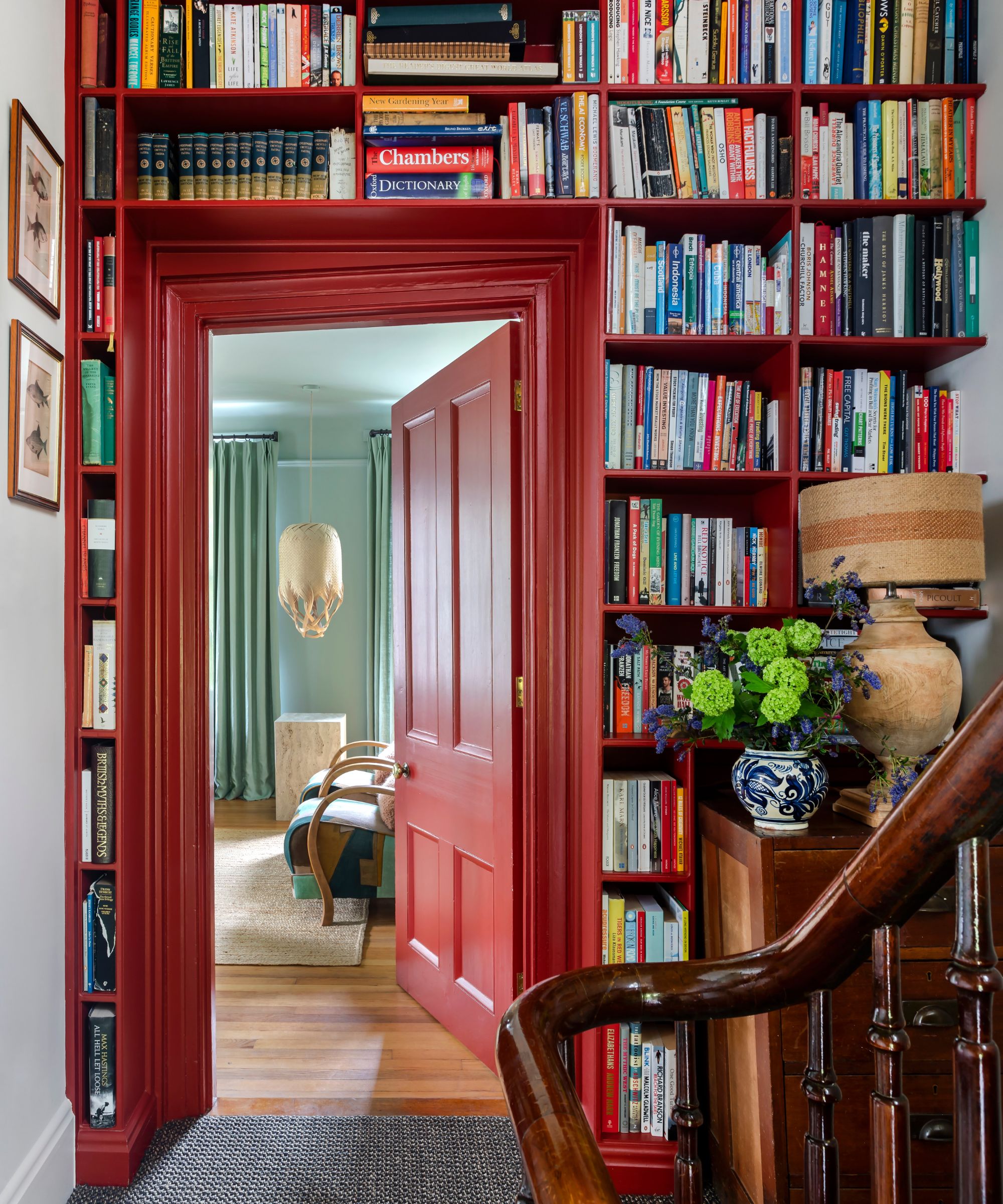 Staircase with built-in bookcase painted red, red painted doorway, a dark mahogany bannister, leading into a living room with blue walls