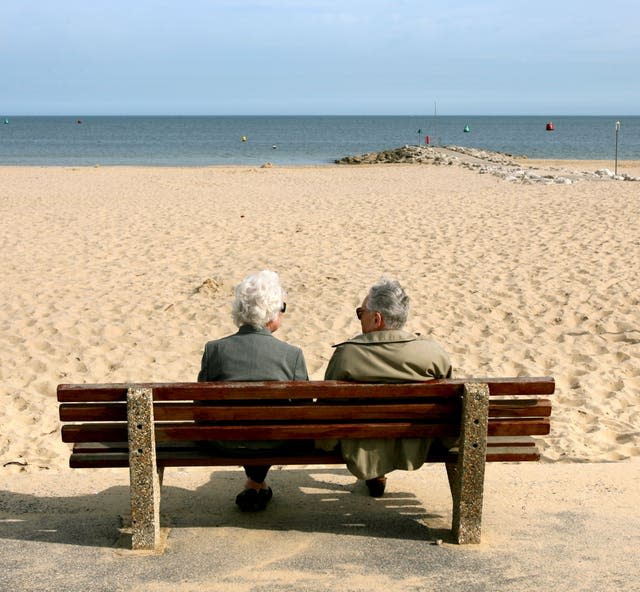 The backs of two pensioners sitting on a bench on a beach, looking out to sea