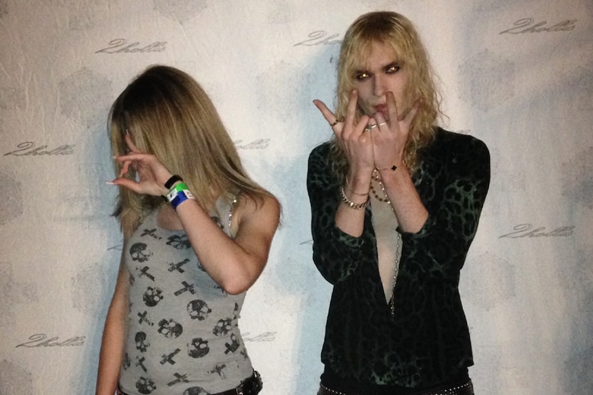 A young woman with face turned, 2hollis standing next to her holding up his fingers in a rock star gesture