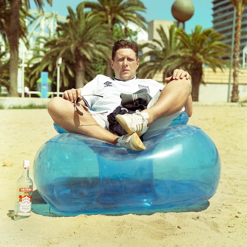 Shaun Ryder on an inflatable chair on a beach in the US in 1999, complete with England football top and a bottle of vodka. Photograph: David Tonge/Getty 