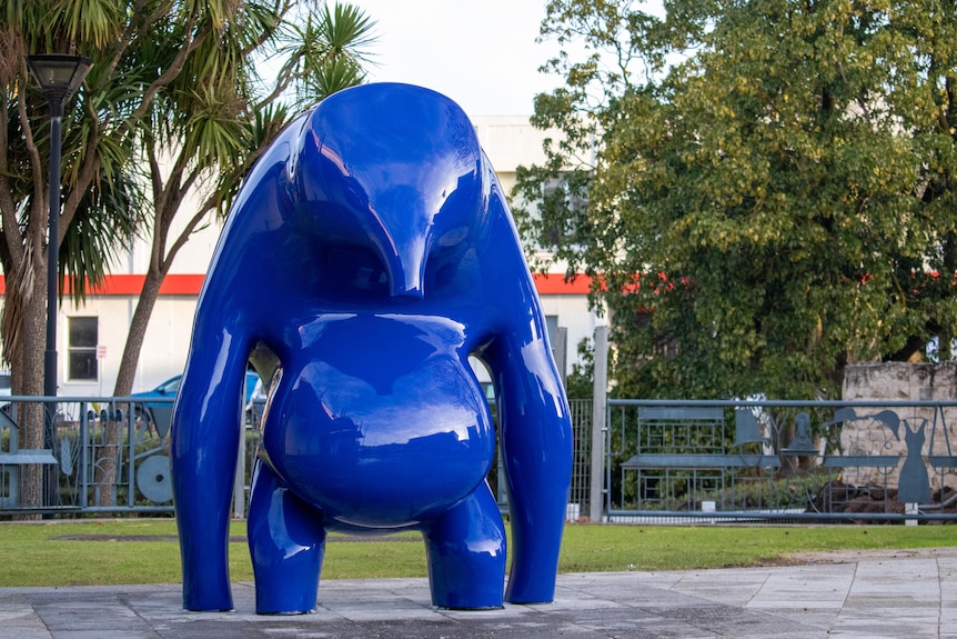 A blue sculpture among pavers and trees.