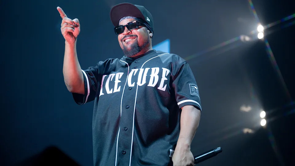 Ice Cube performing on stage, wearing sunglasses and a black jersey with his name.