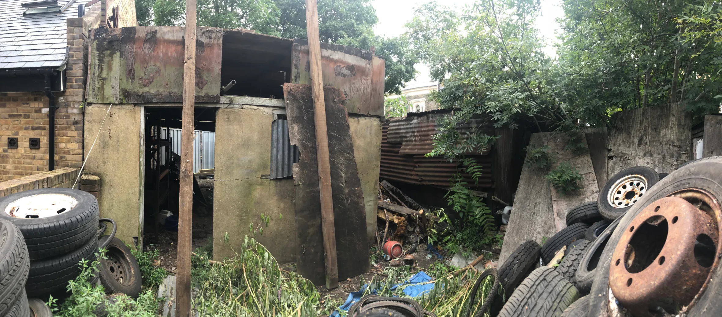 Greenview House before construction, showing an old, rusty structure with overgrown vegetation and discarded tires.