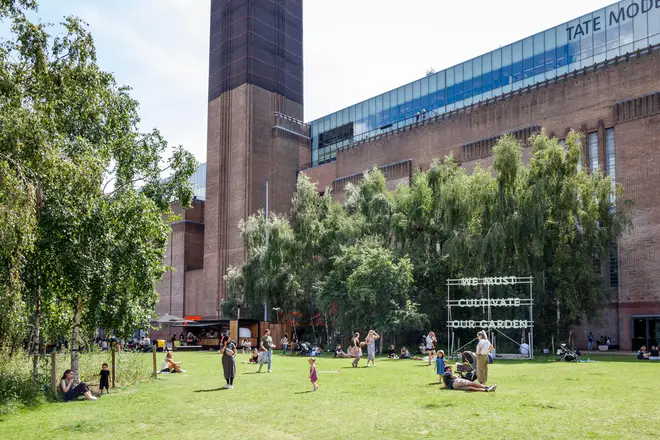 People enjoying the sunshine on the grass outside the Tate modern art gallery at Bankside, London, UK