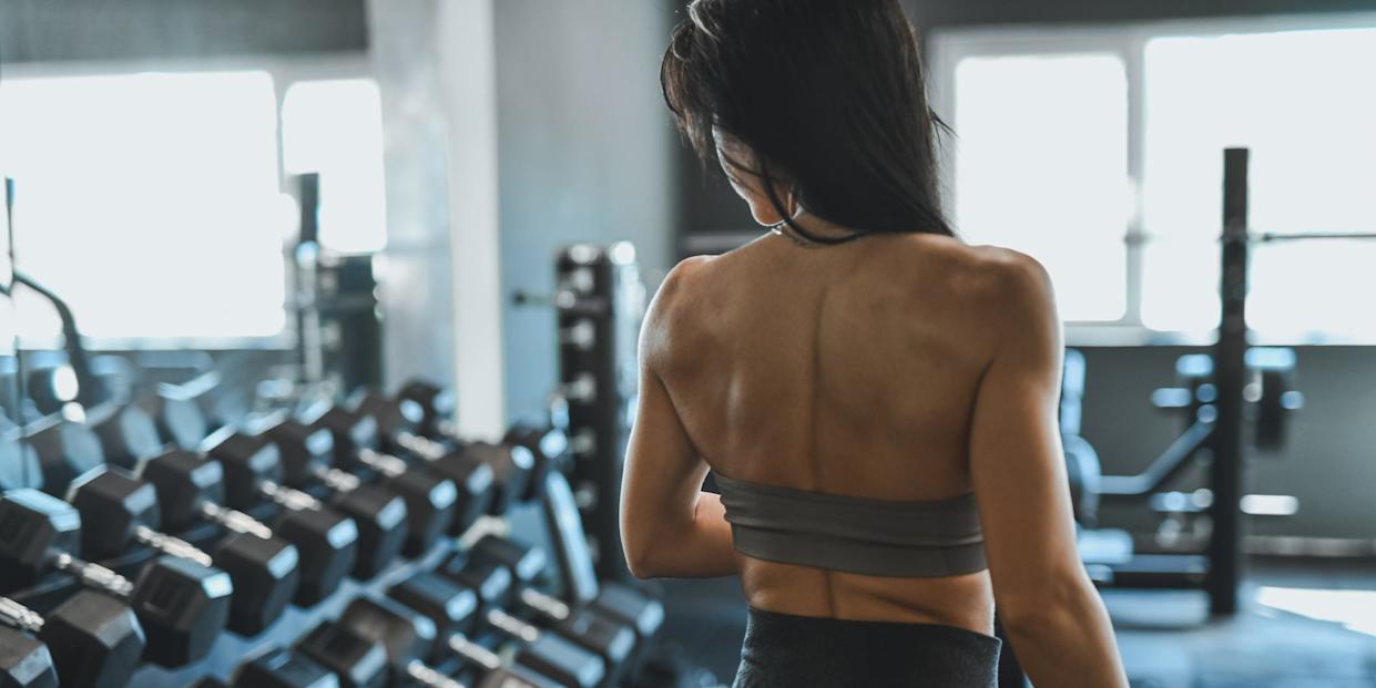 Shredded Woman Working Out in a Modern Gym, Gazing at Dumbbell Rack, Demonstrating Strength and Focus