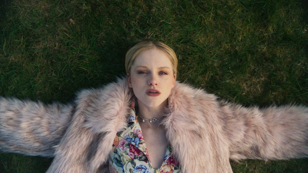 emma laird in bbc mint as shannon laying on the grass with her arms spread out looking pensive.