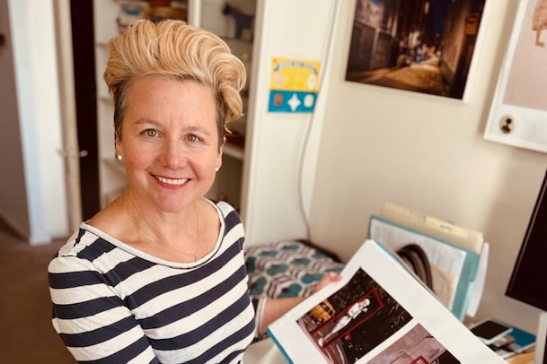A woman with short cropped blonde hair holds a photo album.