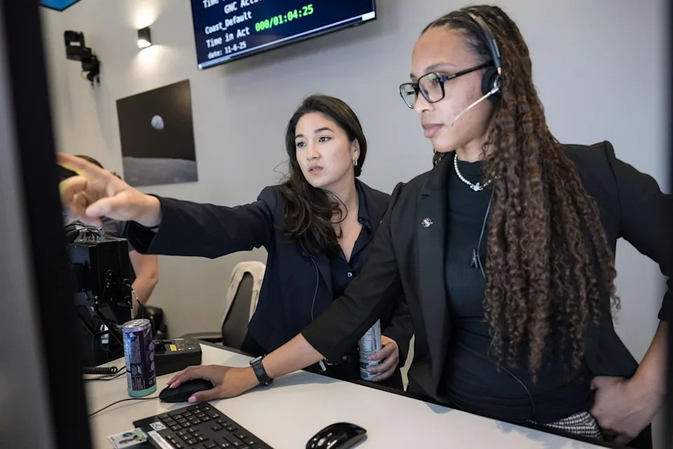 Two women working in a control room, one pointing at a monitor, both wearing headsets and professional attire