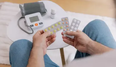 Close-up of elderly man sitting sofa at living room measures blood pressure with device.