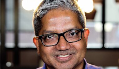 A man with dark, south-asian features, and grey hair with glasses smiling at the camera.
