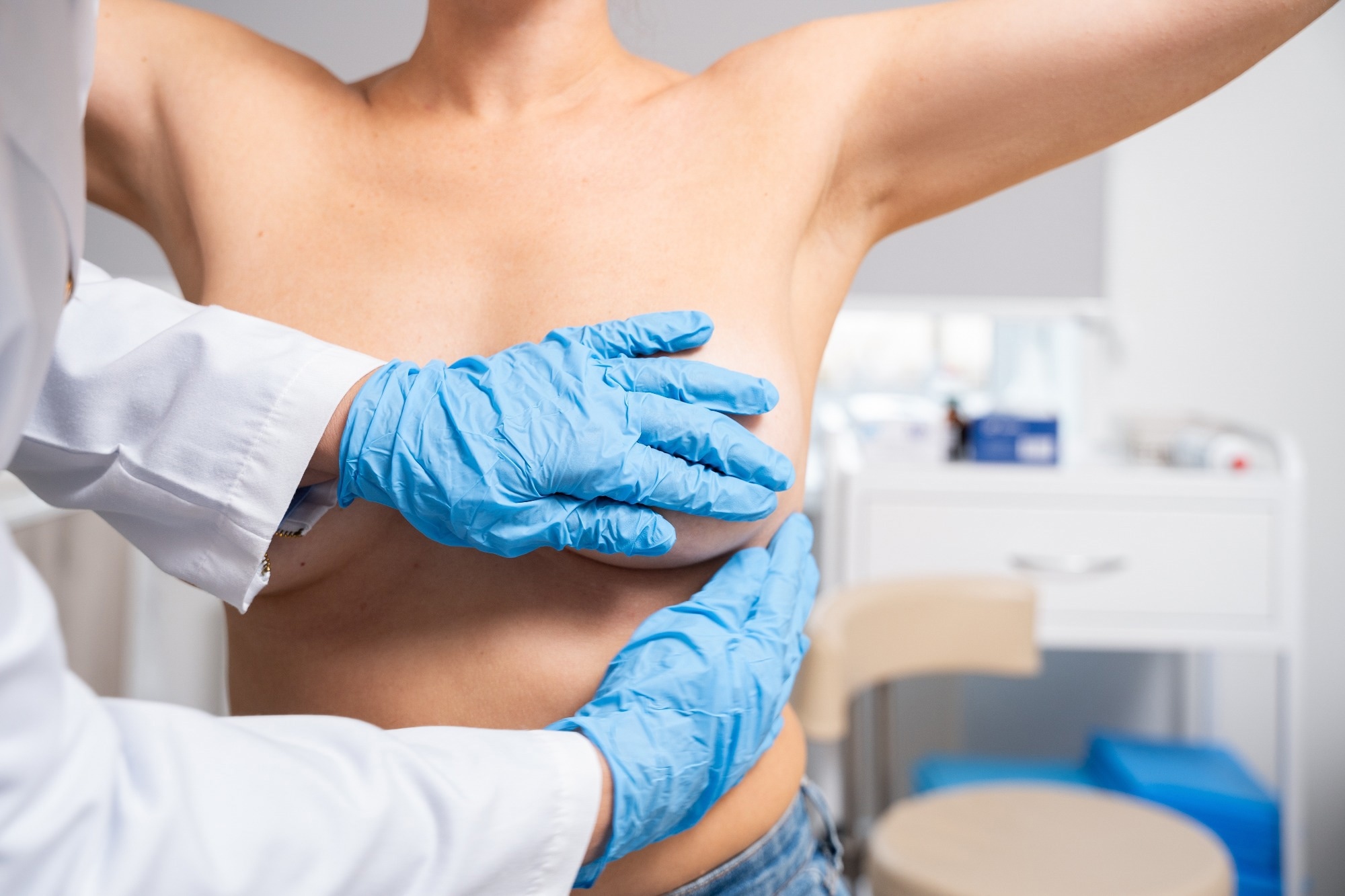 A doctor performs a breast examination on a female patient in a medical setting.