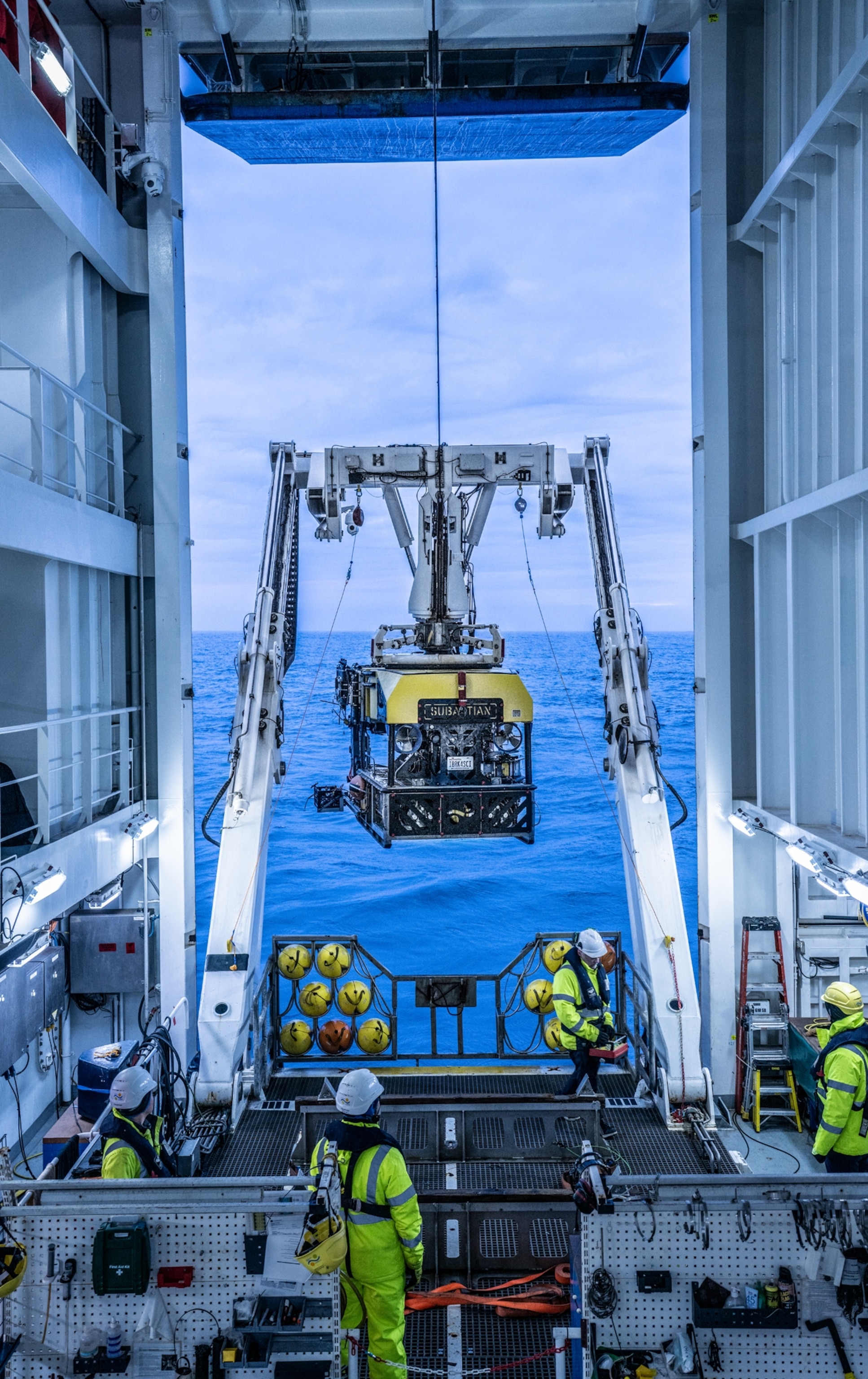 Crue in bright yellow suites watching the apparatus going down from dock into water.