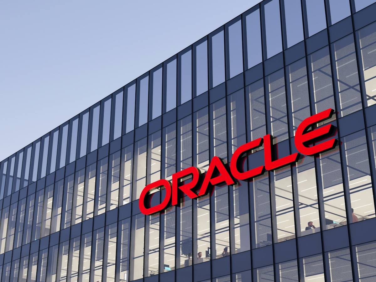 The red Oracle logo on a glass building, against a grey/blue sky.