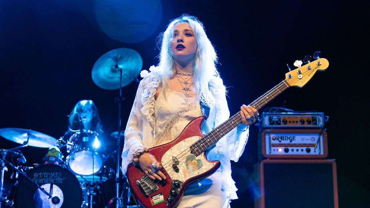 Phoebe Lunny of Lambrini Girls performing onstage while holding a guitar during a concert.