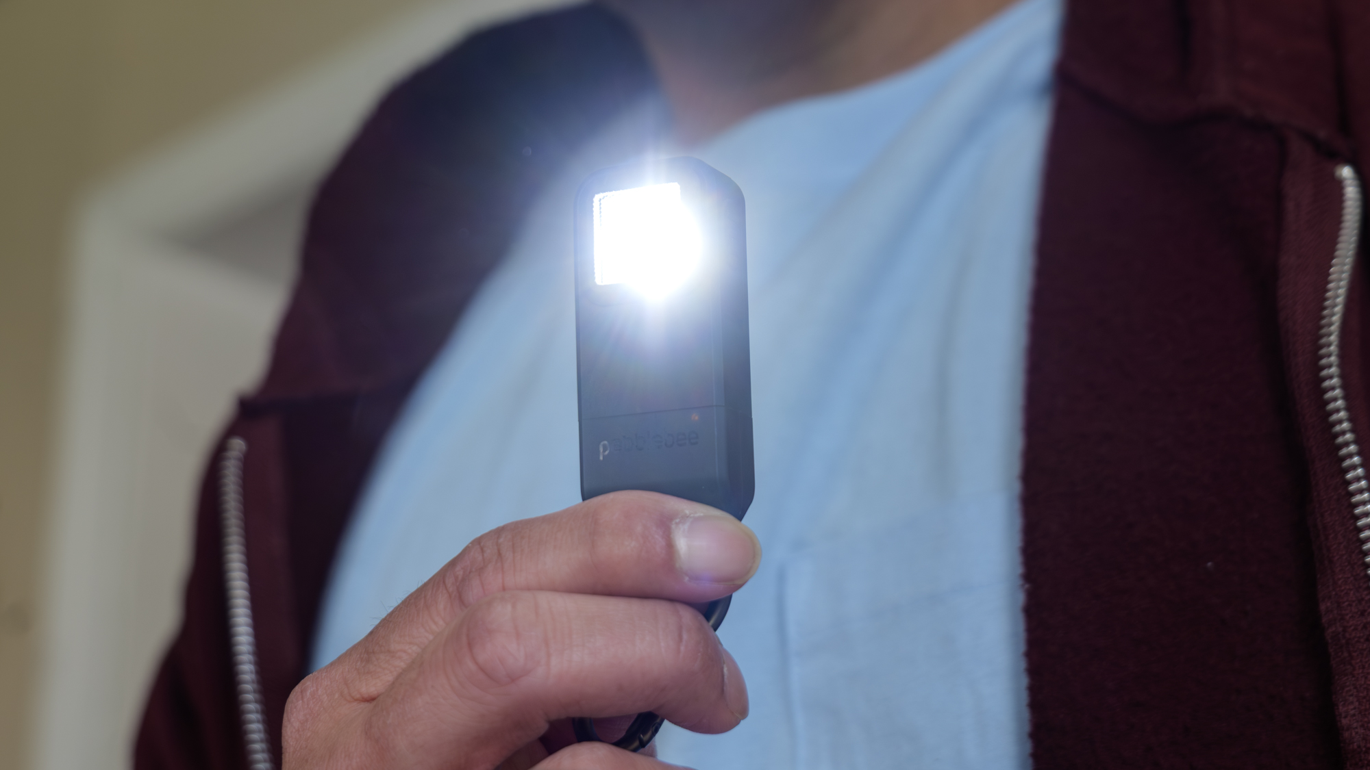 Pebblebee Halo held in the hand with flashlight on.