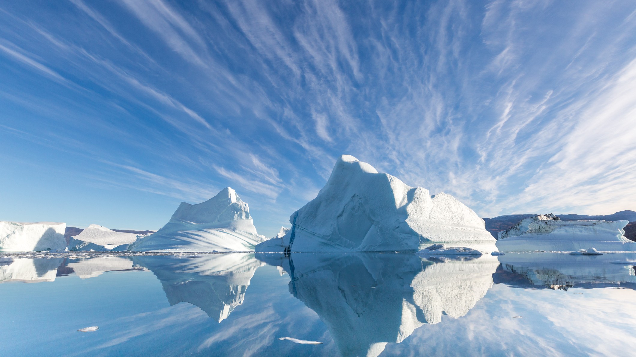 large dramatic icebergs against a blue sky reflected in the water below.