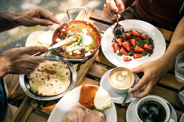 A vibrant brunch spread with shakshuka, granola with strawberries, flatbread, and cappuccino is shared at an outdoor table. A vibrant brunch spread with shakshuka, granola with strawberries, flatbread, and cappuccino is shared at an outdoor table.