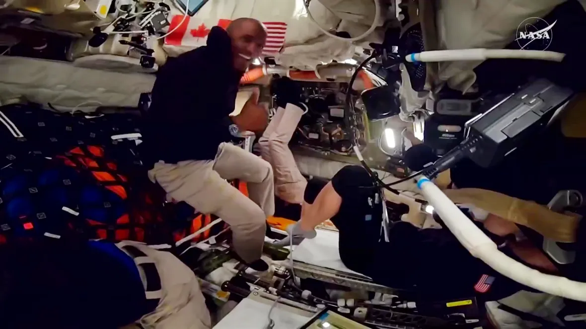 Two astronauts in a spaceship, one giving a thumbs-up.