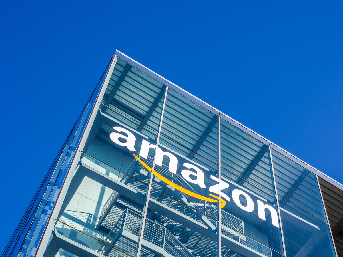 Amazon logo seen on a tall glass building under a blue sky.