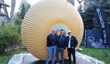 three people in jeans and blazers stand in front of a round crenellated structure in a field