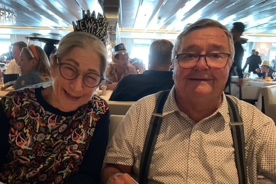 A man and woman with grey hair sit side-by-side in a restaurant smiling.