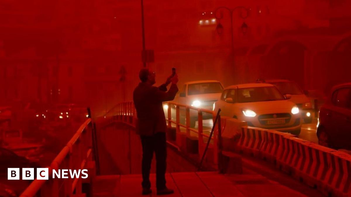 A man takes a picture while cars drive with their headlights on in red air in the city of Heraklion, Crete. Photo: 1 April 2026