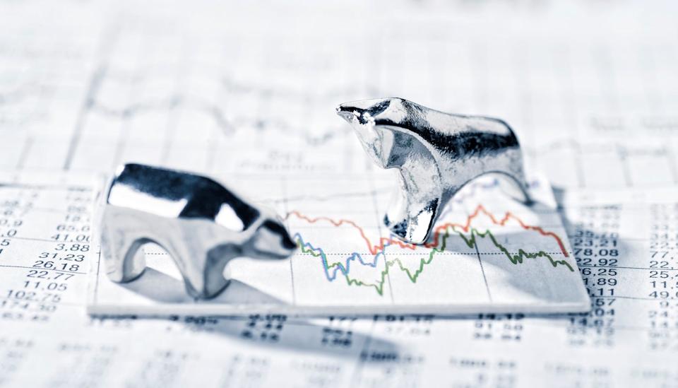 A silver bear and bull stand on a stock price chart thats sits on newsprint.