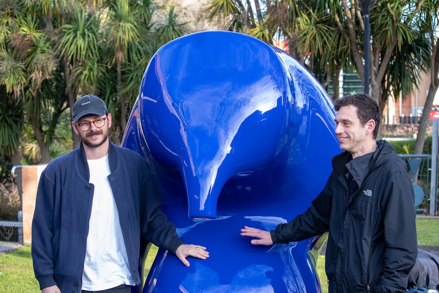 Two men standing either side of a blue sculpture
