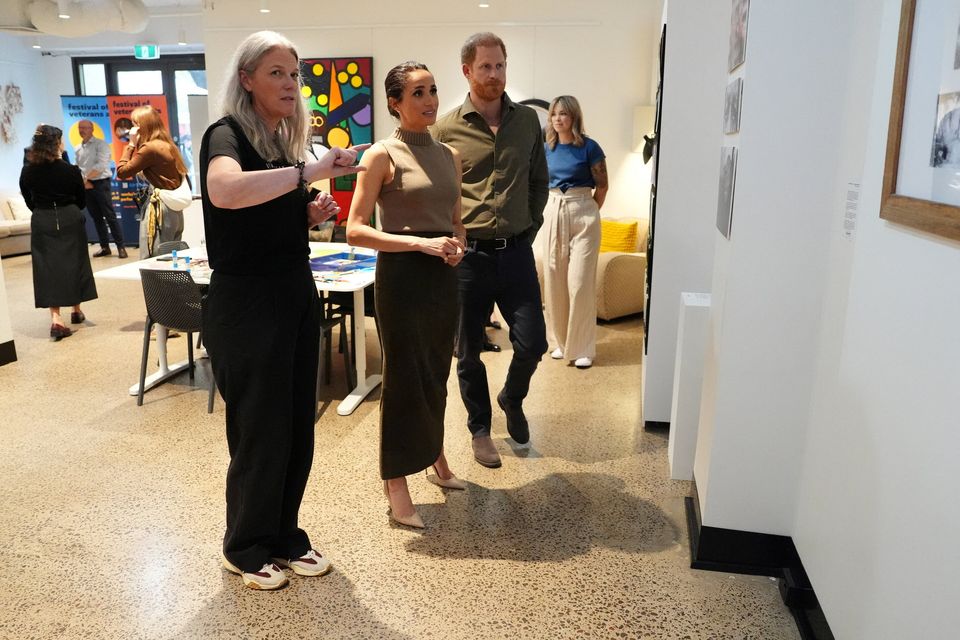 Tanja Johnston, founder of the Australian National Veterans Arts Museum (ANVAM), shows Britain's Prince Harry and Meghan, the Duke and Duchess of Sussex, an exhibit by veterans at ANVAM in Southbank, Melbourne, Australia, April 14, 2026. Jonathan Brady/Pool via REUTERS