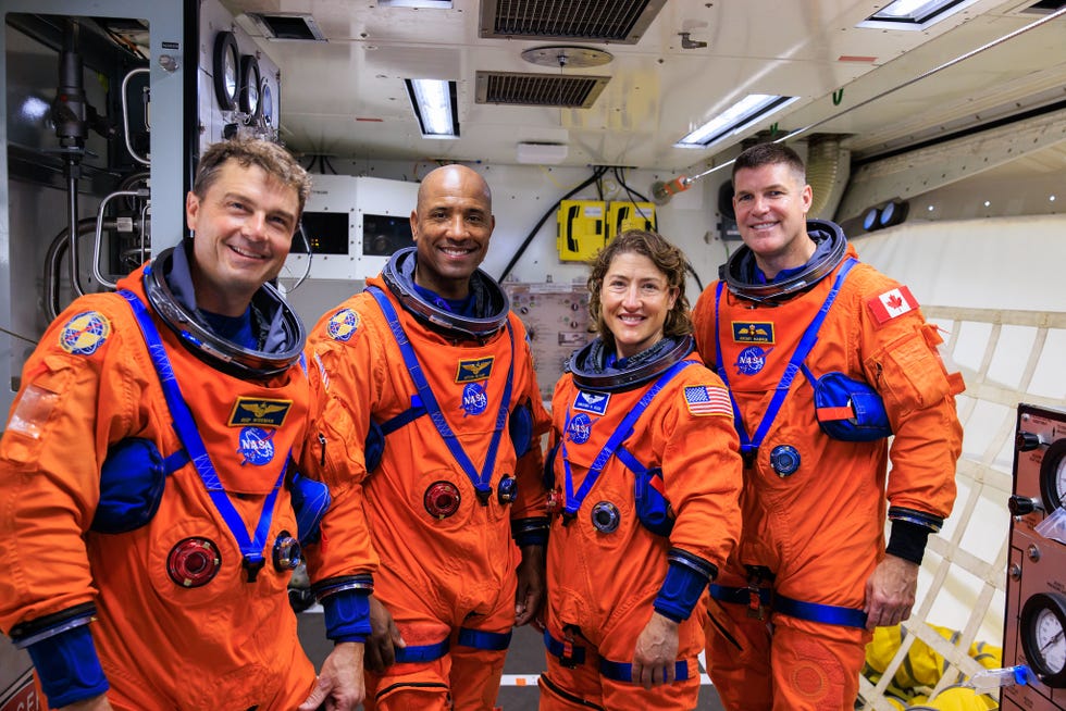 Astronauts in orange space suits inside a spacecraft.