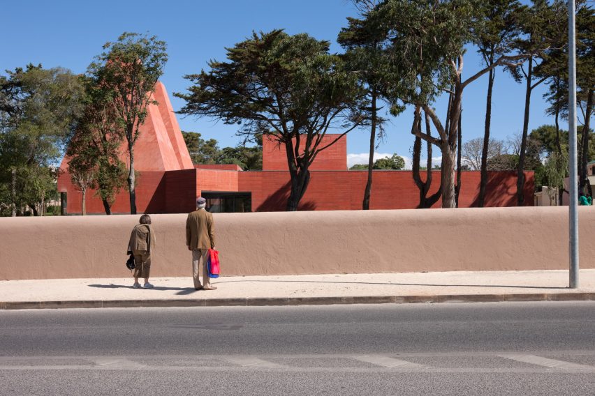 Street view of the museum behind a low wall with visitors looking towards the red concrete building