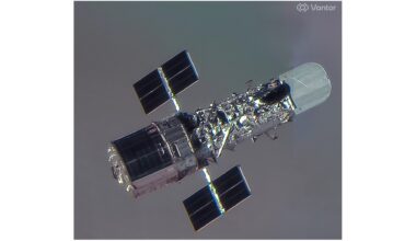 closeup satellite photo of the hubble space telescope, showing it as a shiny silver cylinder with two small solar wings