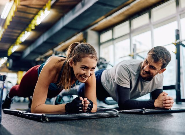 Happy sports couple doing plank exercise while working out in gym. Copy space.